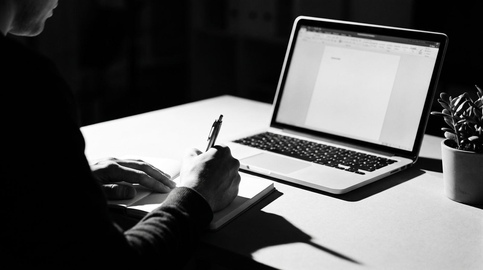 A person working through paperwork by hand beside an open laptop.